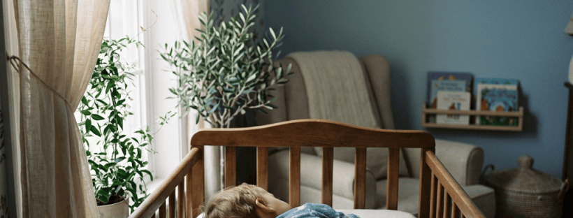 Sleeping child tucked under a knitted blanket in a wooden crib